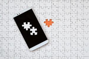 un' moderno grande smartphone con parecchi puzzle elementi su il toccare schermo bugie su un' bianca sega puzzle nel un assemblato stato con mancante elementi foto