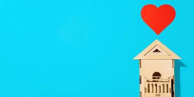 di legno modello di Casa e rosso carta cuore su leggero blu sfondo, piatto posizione. casa dolce casa. concettuale bandiera superiore Visualizza, copia spazio. foto