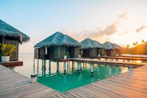 tramonto sull'isola delle maldive, resort di ville sull'acqua di lusso e molo in legno. bel cielo e nuvole e sfondo della spiaggia per le vacanze estive e il concetto di viaggio foto