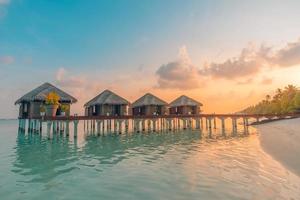 tramonto sull'isola delle maldive, resort di ville sull'acqua di lusso e molo in legno. bel cielo e nuvole e sfondo della spiaggia per le vacanze estive e il concetto di viaggio foto