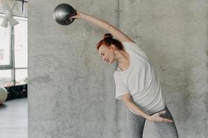giovane donna dai capelli rossi atletica che esegue esercizio di sbarra con piccolo fitball foto