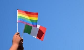 Italia bandiera e arcobaleno bandiera, lgbt simbolo, Tenere nel mani, cielo blu sfondo, concetto per lgbt celebrazione nel Italia e in giro il mondo nel orgoglio mese, giugno, morbido e selettivo messa a fuoco, copia spazio. foto