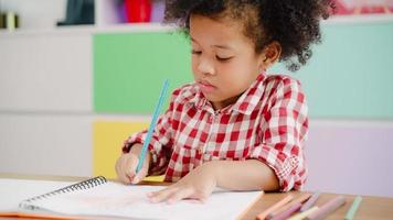 africano bambini disegno e fare compiti a casa nel aula, giovane ragazza contento divertente studia e giocare pittura su carta a elementare scuola. ragazzo disegno e pittura a scuola concetto. foto