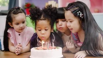 gruppo di bambini celebrare compleanno festa nel aula, multietnico giovane ragazzi e ragazze contento rendere un' desiderio soffio su candele su compleanno torta a scuola. bambini celebrare compleanno a scuola concetto. foto