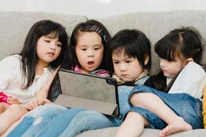 gruppo di bambini utilizzando tavoletta nel aula, multietnico giovane ragazzi e ragazze contento utilizzando tecnologia per studia e giocare Giochi a elementare scuola. bambini uso tecnologia per formazione scolastica concetto. foto