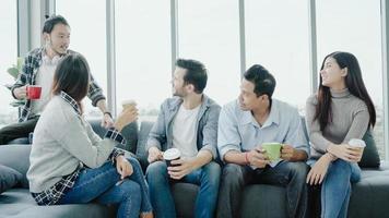 diversità di giovani gruppo squadra in possesso di tazze di caffè e discutere di qualcosa con un sorriso mentre era seduto sul divano in ufficio. pausa caffè presso l'ufficio creativo. foto