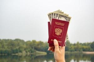 un passaporto straniero e dollari in mano, sullo sfondo della natura. foto