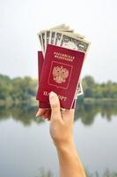 un passaporto straniero e dollari in mano, sullo sfondo della natura. foto