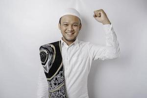 un' contento giovane asiatico musulmano uomo con un' preghiera tappeto su il suo spalla mostrando un' riuscito espressione isolato di bianca sfondo foto