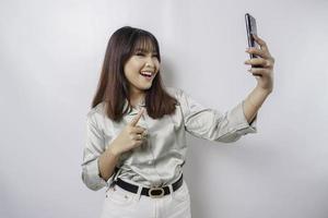 un' ritratto di un' contento asiatico donna indossare un' saggio verde camicia e Tenere sua Telefono, isolato di bianca sfondo foto