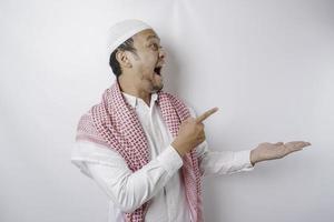 scioccato asiatico musulmano uomo puntamento a il copia spazio accanto lui, isolato di bianca sfondo foto