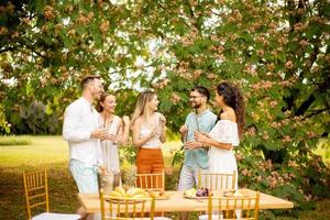 gruppo di contento giovane persone applauso con fresco limonata e mangiare frutta nel il giardino foto