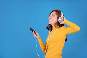 allegro asiatico donna indossare cuffie ascoltando per musica su smartphone su un' leggero blu sfondo nel il studio. foto