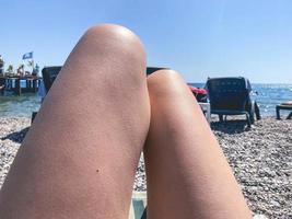 bellissimo giovane sottile donna gambe prendere il sole su il spiaggia vicino il mare. foto