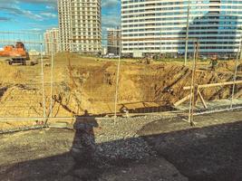 costruzione di un' nuovo la zona di il città. alto case sotto costruzione recintato con fossato e sabbia, metallo alto struttura foto