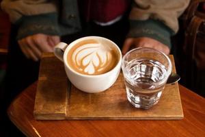 tazza di caldo cappuccino e bicchiere di acqua su il di legno tavolo nel un' bar. foto