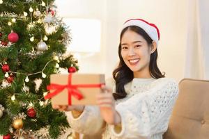 Natale celebrazione concetto, giovane asiatico donna nel Santa cappello sorridente e Tenere Natale regalo foto