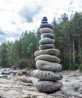 un' piramide di spoglio pietre impilati su superiore di ogni Altro. pietre impilati nel il forma di un' piramide su il Riva del fiume contro il sfondo di montagne come equilibrio e equilibrio nel natura, zen, buddismo. foto