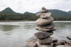 un' piramide di spoglio pietre impilati su superiore di ogni Altro. pietre impilati nel il forma di un' piramide su il Riva del fiume contro il sfondo di montagne come equilibrio e equilibrio nel natura, zen, buddismo. foto