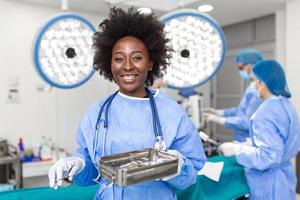 ritratto di africano americano donna chirurgo in piedi nel operativo camera, pronto per opera su un' paziente. femmina medico lavoratore nel chirurgico uniforme nel operazione Teatro.
