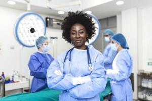 ritratto di contento africano americano donna chirurgo in piedi nel operativo camera, pronto per opera su un' paziente. femmina medico lavoratore medico nel chirurgico uniforme nel operazione Teatro.