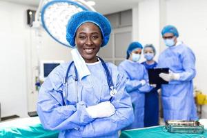ritratto di chirurgo in piedi nel operativo camera, pronto per opera su un' paziente. africano americano femmina medico lavoratore chirurgico uniforme nel operazione Teatro. foto