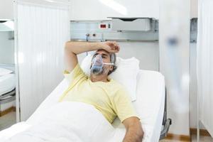 ritratto di pensionato anziano uomo respirazione lentamente con ossigeno maschera durante coronavirus covid-19 scoppio. vecchio malato uomo dire bugie nel ospedale letto, ottenere trattamento per mortale infezione foto