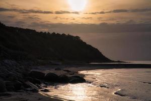 tramonto su il danese costa. spiaggia, onde. collina con alberi nel sfondo. paesaggio foto