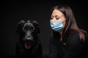 ritratto di un' labrador cane da riporto cane nel un' protettivo medico maschera con un' femmina proprietario. foto