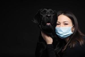 ritratto di un' labrador cane da riporto cane nel un' protettivo medico maschera con un' femmina proprietario. foto