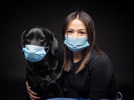 ritratto di un' labrador cane da riporto cane nel un' protettivo medico maschera con un' femmina proprietario. foto