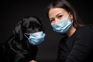 ritratto di un' labrador cane da riporto cane nel un' protettivo medico maschera con un' femmina proprietario. foto