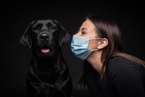 ritratto di un' labrador cane da riporto cane nel un' protettivo medico maschera con un' femmina proprietario. foto