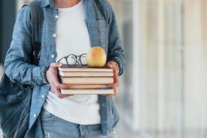 vicino su Visualizza di ,ale giovane alunno nel jeans Abiti quello è nel corridoio di un' Università con libri con Mela su esso nel mani foto