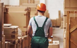 giovane maschio lavoratore nel uniforme è nel il magazzino con pallet camion foto