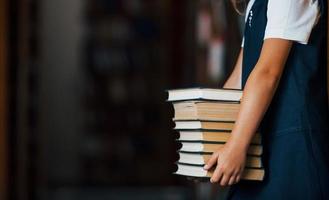 particella Visualizza di poco ragazza detiene molti libri nel mani nel il biblioteca foto
