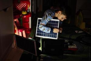 ragazzo giocando a casa durante un' oscuramento utilizzando alternativa illuminazione con solare pannello. foto