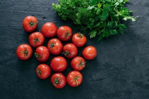 vista dall'alto di pomodori freschi maturi rossi con prezzemolo verde su sfondo scuro. vitamine e concetto di nutrizione. copia spazio. cibo crudo foto