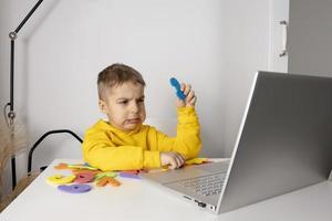 poco ragazzo apprendimento alfabeto e numeri in linea, con il computer portatile a casa. bambino è triste e stanco. negativo emozioni, fatica, mentale i problemi. homeschooling e distanza formazione scolastica per bambini. foto