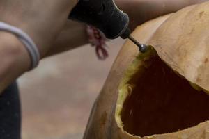 giovane uomo con un' trapano o dremel perforazione un' zucca per Halloween foto