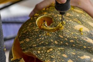 giovane uomo con un' trapano o dremel perforazione un' zucca per Halloween foto