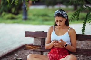 donna utilizzando un' smartphone nel parco seduta su un' panchina foto