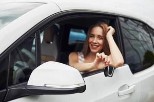 sensazione contento. femmina autista mostrando sua chiavi mentre si siede dentro di automobile foto