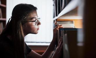 ricerca per giusto informazione. contro finestra. femmina alunno è nel biblioteca quello pieno di libri. concezione di formazione scolastica foto