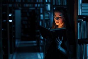 leggero a partire dal il libro nel buio camera. immaginazione concezione. femmina alunno è nel biblioteca quello pieno di libri. concezione di formazione scolastica foto