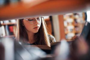 Visualizza attraverso il scaffali. femmina alunno è nel biblioteca quello pieno di libri. concezione di formazione scolastica foto