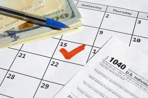 1040 individuale reddito imposta ritorno vuoto con credito carta su dollaro fatture e penna su calendario pagina con segnato 15 aprile foto