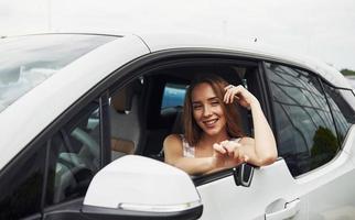 sensazione contento. femmina autista mostrando sua chiavi mentre si siede dentro di automobile foto
