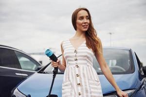 donna su il elettrico macchine caricare stazione a giorno. marca nuovo veicolo foto