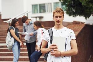 tipo in posa per il telecamera. gruppo di giovane studenti nel casuale Abiti vicino Università a giorno foto